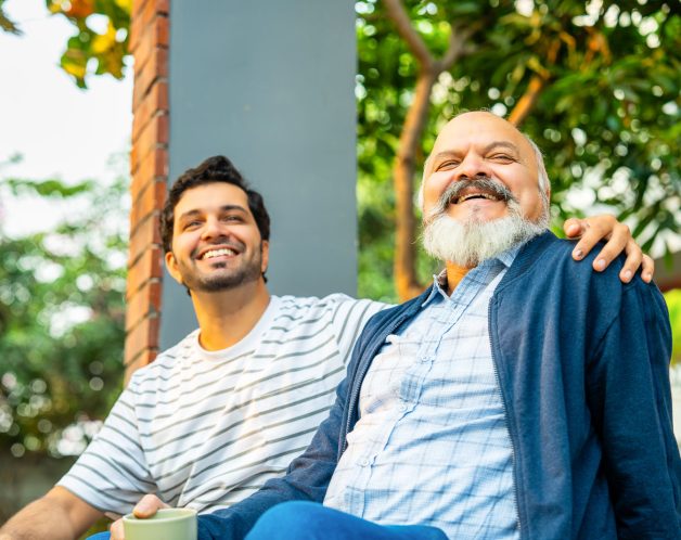 Indian Asian Happy Old Aged Father and Young Adult Son Sitting on Porch of Home Outdoors, Engaging in Heartfelt Conversation and Laughing Together, Showcasing Father-Son Bonding